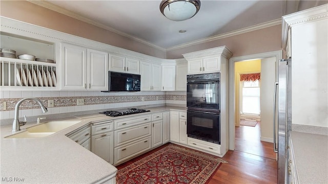 kitchen featuring light countertops, ornamental molding, wood finished floors, black appliances, and a sink