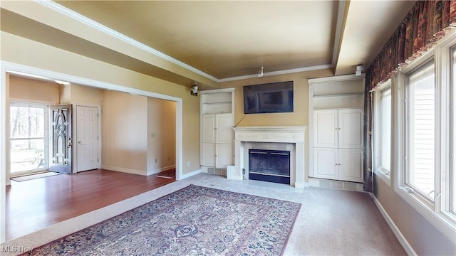 unfurnished living room with a wealth of natural light, a fireplace with flush hearth, crown molding, and baseboards