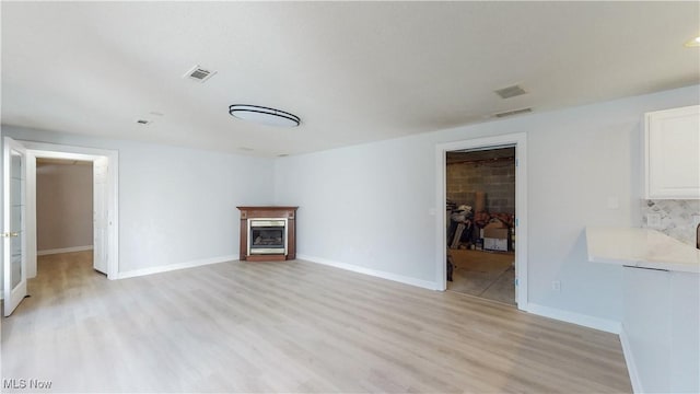 unfurnished living room featuring light wood finished floors, visible vents, a fireplace, and baseboards