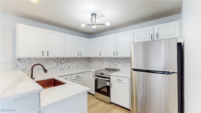 kitchen featuring a sink, tasteful backsplash, white cabinetry, appliances with stainless steel finishes, and a peninsula