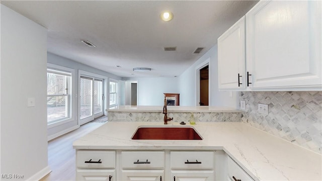 kitchen with light stone counters, tasteful backsplash, visible vents, and a sink