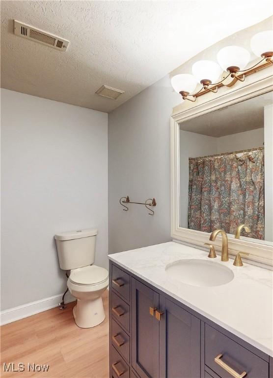 bathroom with visible vents, toilet, vanity, wood finished floors, and a textured ceiling