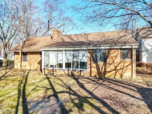 rear view of house with entry steps, brick siding, a chimney, and a lawn