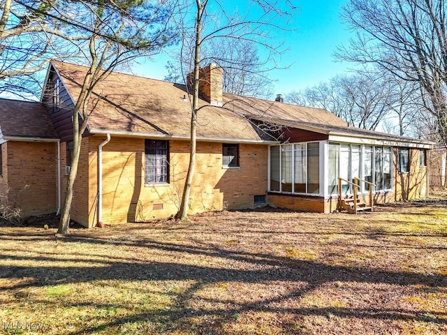 rear view of house featuring a sunroom, a shingled roof, crawl space, brick siding, and a chimney