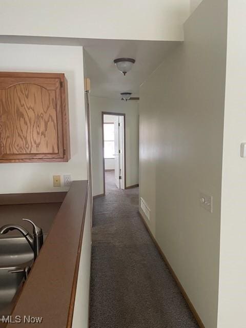 hallway featuring a sink, visible vents, baseboards, and dark colored carpet