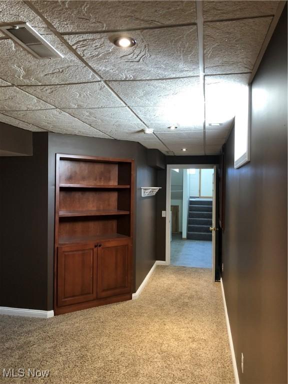 hall featuring visible vents, baseboards, a drop ceiling, stairway, and carpet floors