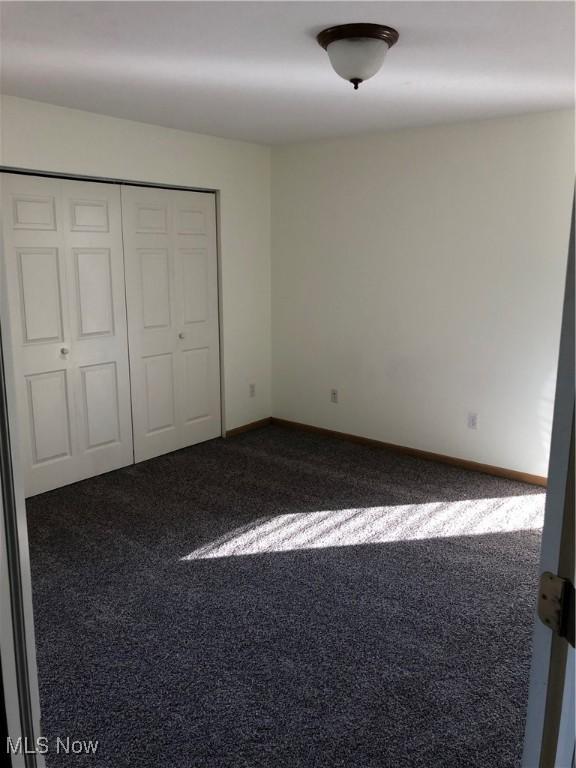 unfurnished bedroom featuring dark colored carpet, a closet, and baseboards