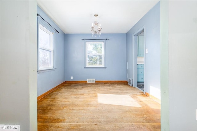 unfurnished room with a notable chandelier, wood finished floors, visible vents, and baseboards