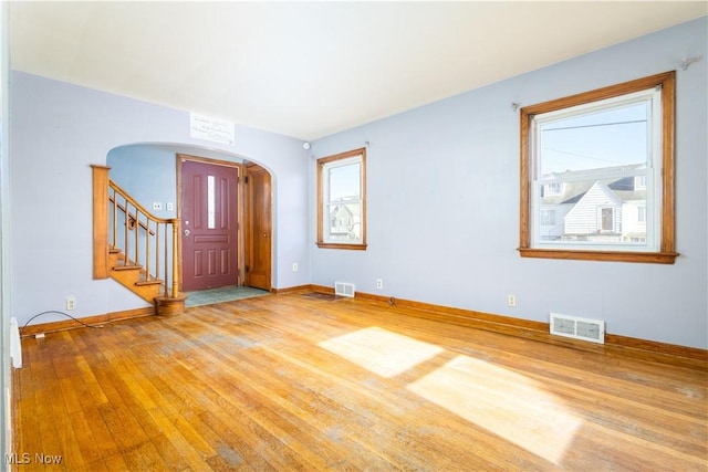 unfurnished room with wood finished floors, visible vents, arched walkways, and a wealth of natural light