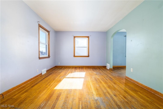 empty room with visible vents, arched walkways, light wood-style floors, and baseboards