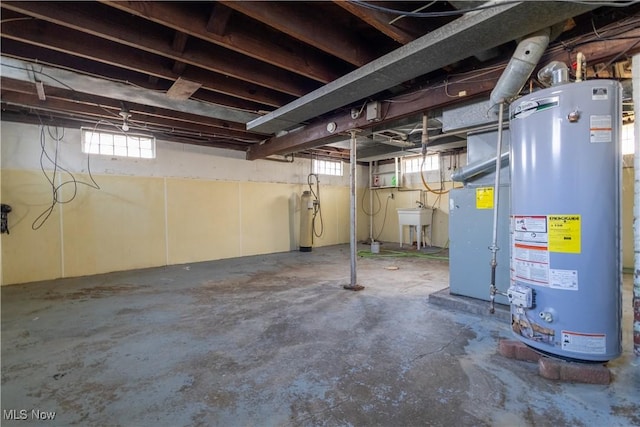 basement featuring heating unit, plenty of natural light, water heater, and a sink