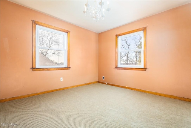 carpeted empty room featuring a chandelier and baseboards