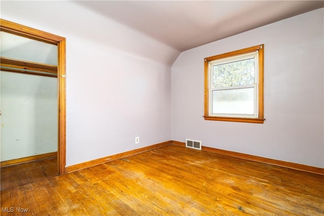 unfurnished bedroom with visible vents, baseboards, lofted ceiling, a closet, and wood-type flooring