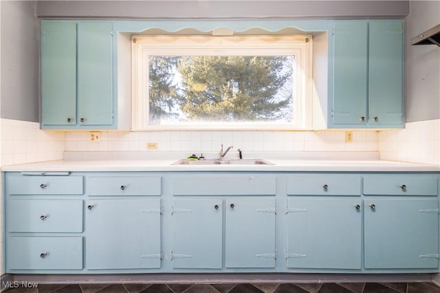 kitchen with backsplash, blue cabinetry, light countertops, and a sink