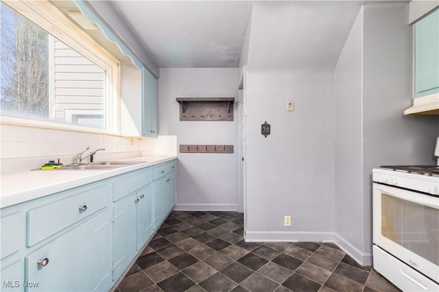 kitchen featuring gas range gas stove, light countertops, under cabinet range hood, blue cabinets, and tasteful backsplash