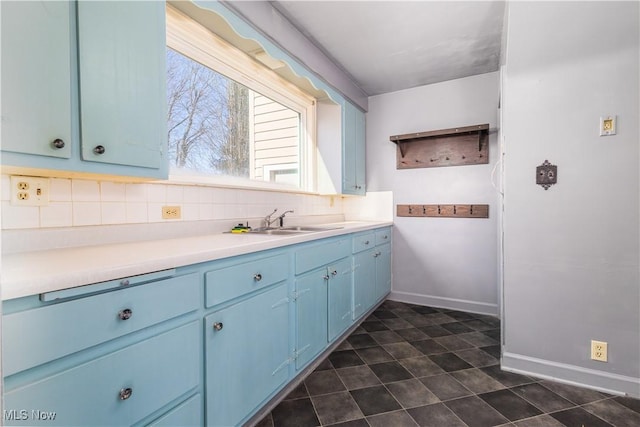 kitchen with blue cabinets, a sink, backsplash, light countertops, and baseboards