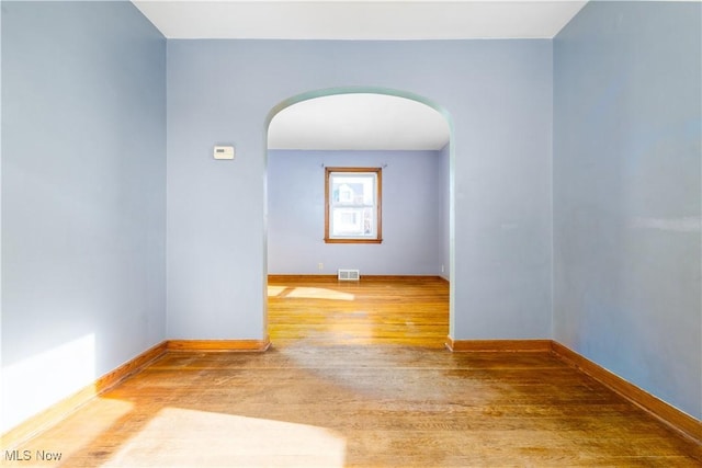 spare room with wood finished floors, visible vents, arched walkways, and baseboards