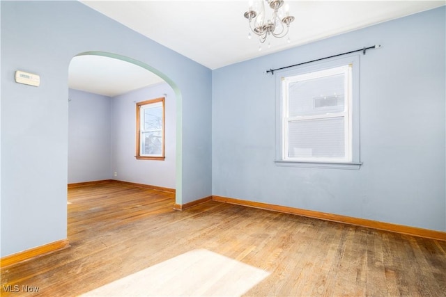 unfurnished room with baseboards, arched walkways, wood finished floors, and a chandelier