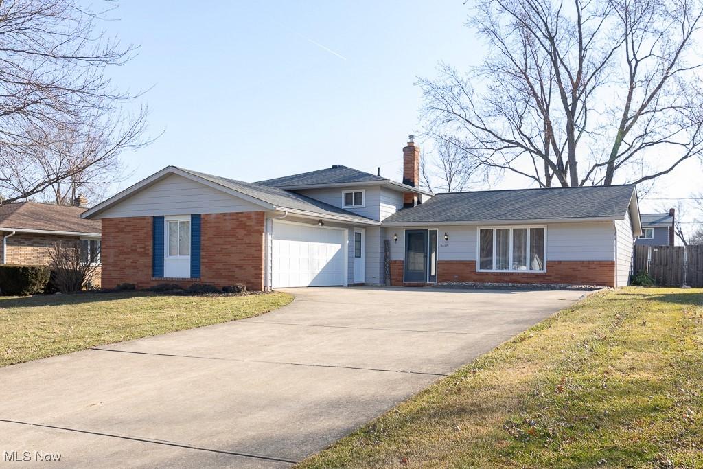 ranch-style house with a front yard, driveway, a chimney, a garage, and brick siding