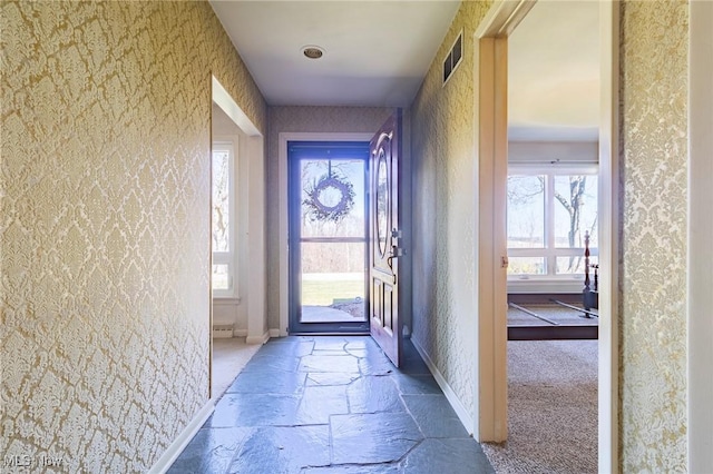 entryway featuring visible vents, baseboards, stone tile flooring, and wallpapered walls