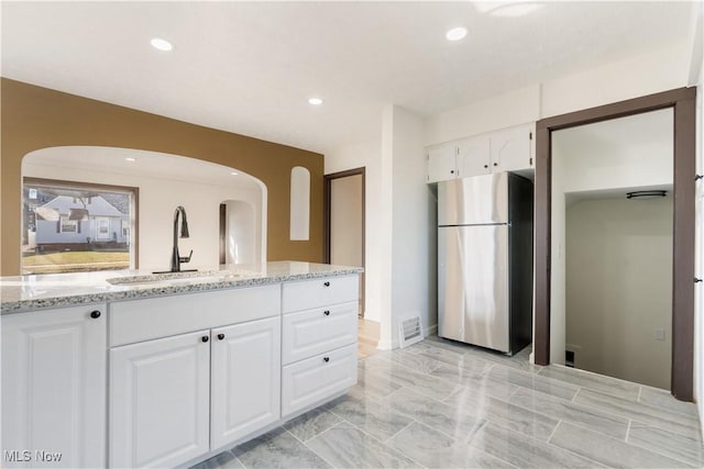 kitchen featuring visible vents, a sink, white cabinetry, freestanding refrigerator, and light stone countertops