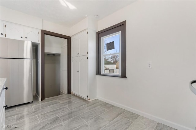 kitchen with baseboards, white cabinetry, light countertops, and freestanding refrigerator