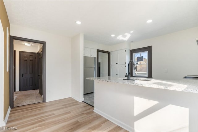 kitchen featuring light stone countertops, freestanding refrigerator, a sink, white cabinetry, and light wood-type flooring