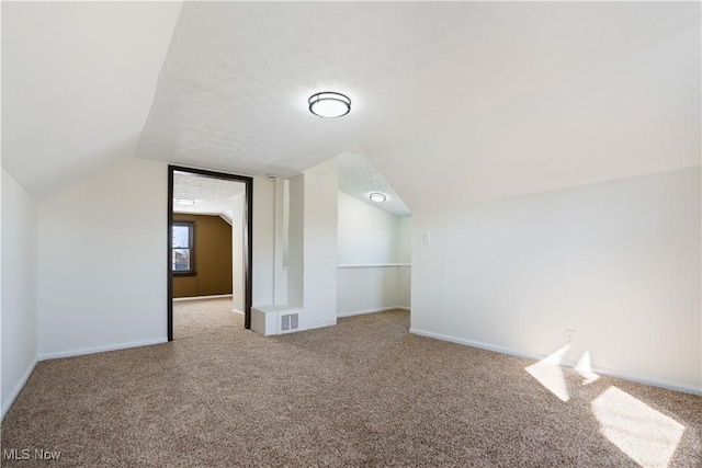 additional living space with visible vents, carpet floors, baseboards, and vaulted ceiling