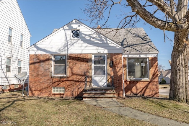 bungalow-style home with entry steps, a front lawn, brick siding, and a shingled roof