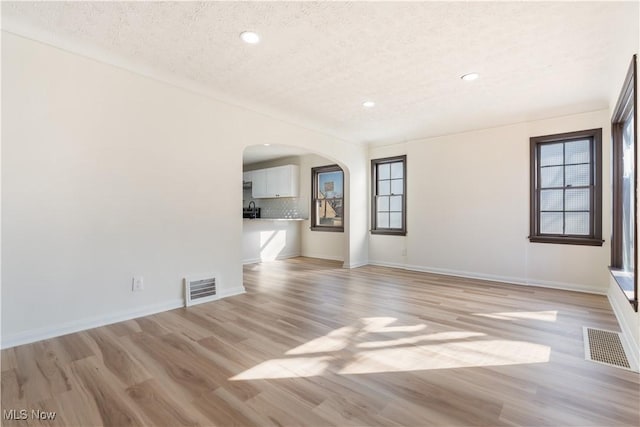 unfurnished living room featuring arched walkways, visible vents, light wood finished floors, and a textured ceiling