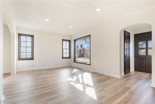 spare room featuring arched walkways, light wood-style flooring, and a textured ceiling