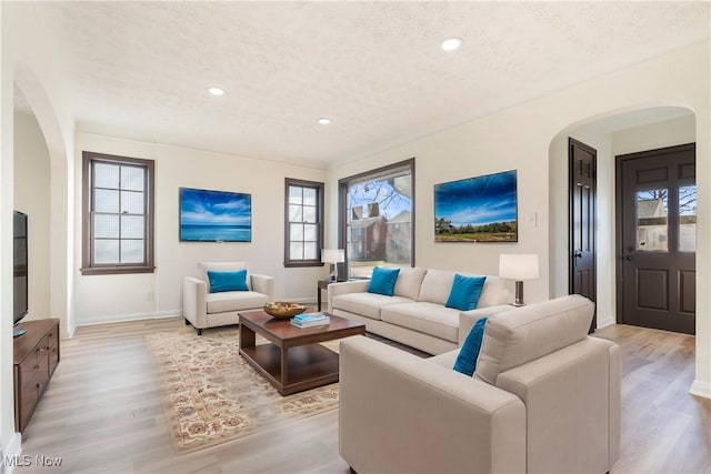 living room with arched walkways, a healthy amount of sunlight, light wood-style floors, and a textured ceiling