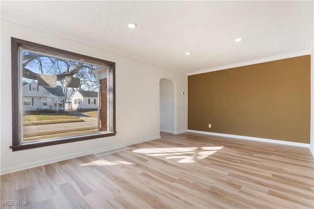 empty room featuring visible vents, arched walkways, baseboards, and light wood finished floors