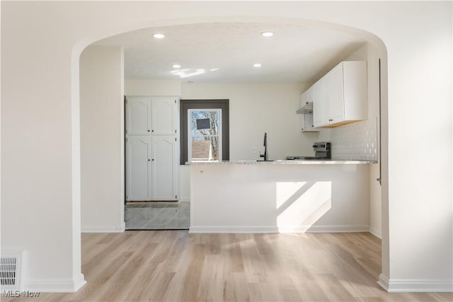 kitchen featuring a peninsula, stainless steel electric stove, arched walkways, white cabinetry, and light wood-type flooring