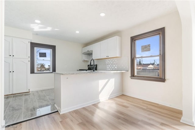 kitchen with a peninsula, a healthy amount of sunlight, white cabinets, and light countertops