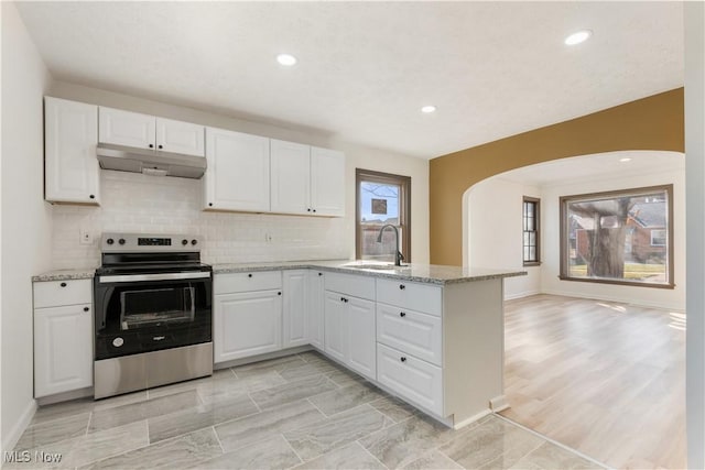 kitchen with electric range, under cabinet range hood, a sink, arched walkways, and a peninsula