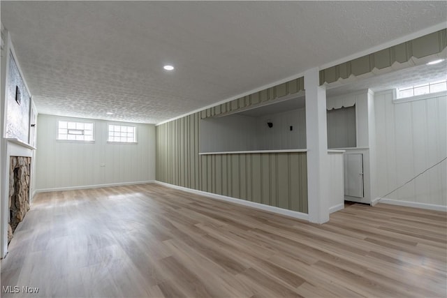 basement featuring a fireplace, a textured ceiling, baseboards, and wood finished floors