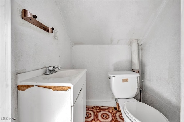 half bath featuring toilet, lofted ceiling, a textured wall, tile patterned floors, and vanity