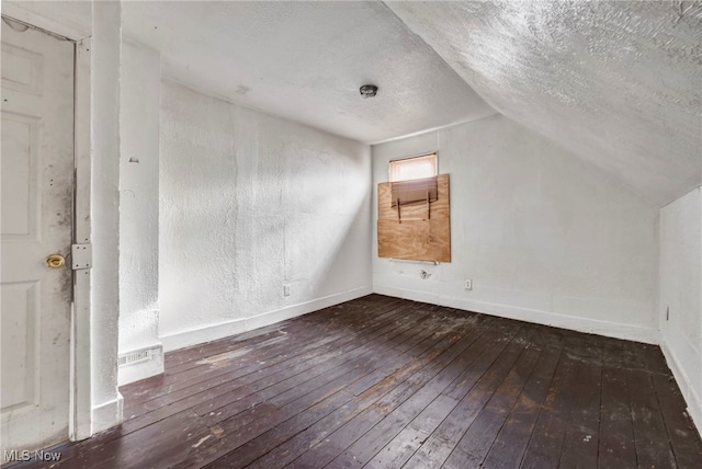 additional living space with vaulted ceiling, a textured ceiling, baseboards, and hardwood / wood-style flooring