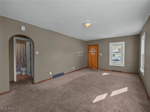 carpeted spare room with visible vents, arched walkways, and baseboards