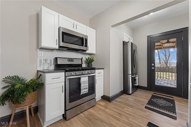 kitchen with dark countertops, white cabinetry, stainless steel appliances, light wood finished floors, and decorative backsplash