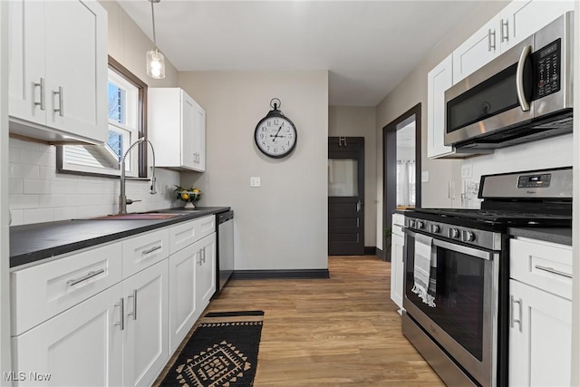 kitchen with a sink, dark countertops, white cabinetry, appliances with stainless steel finishes, and light wood finished floors