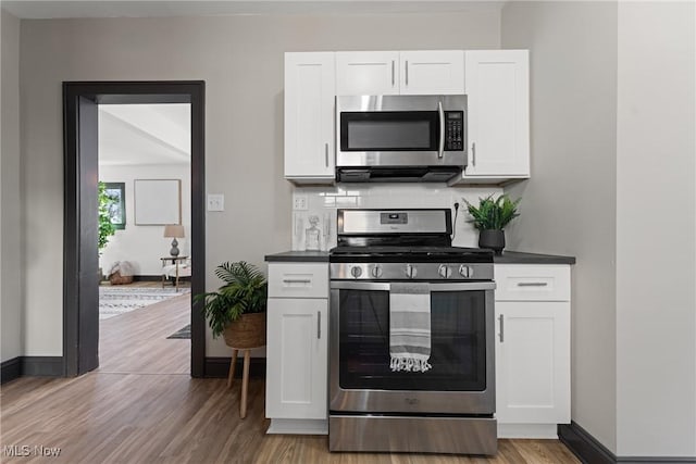 kitchen with backsplash, dark countertops, stainless steel appliances, white cabinets, and baseboards