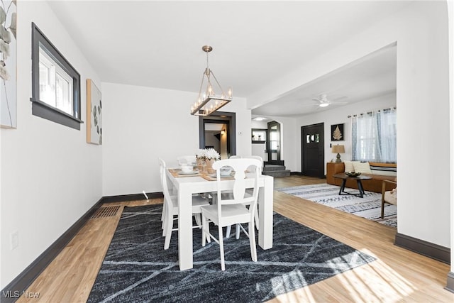 dining area featuring ceiling fan with notable chandelier, baseboards, and wood finished floors