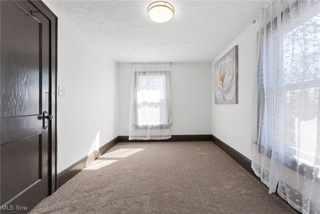 empty room with carpet, baseboards, and a textured ceiling