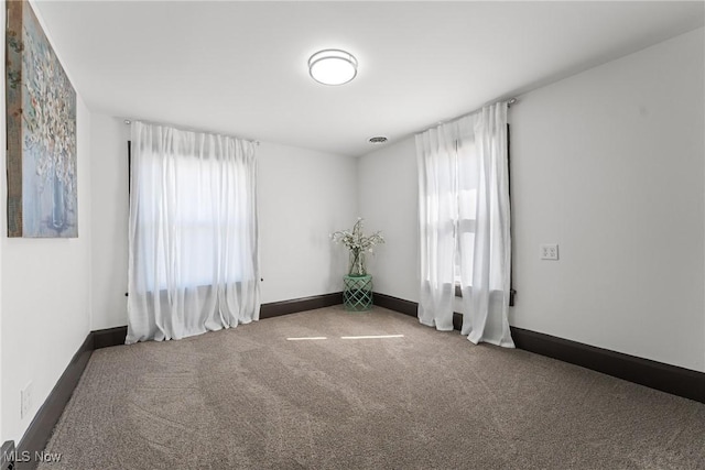 carpeted empty room with visible vents, a healthy amount of sunlight, and baseboards