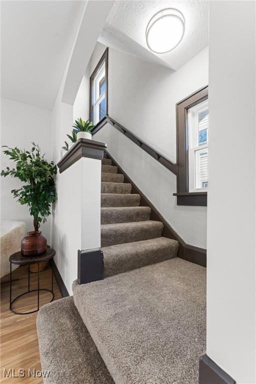 stairway featuring a textured ceiling, baseboards, and wood finished floors