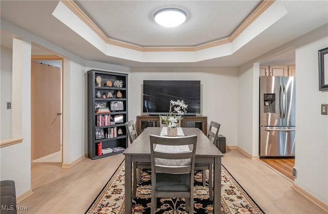 dining room featuring a tray ceiling, crown molding, light wood-type flooring, and baseboards