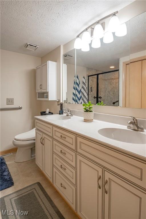 bathroom featuring a textured ceiling, toilet, a stall shower, and a sink