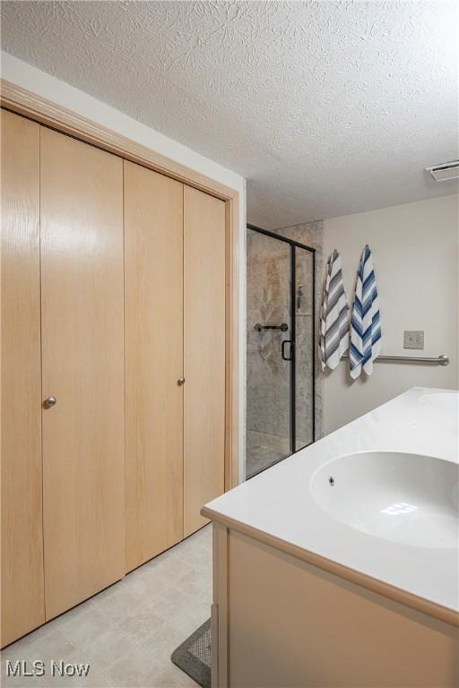 full bathroom featuring a textured ceiling, a stall shower, visible vents, and a sink